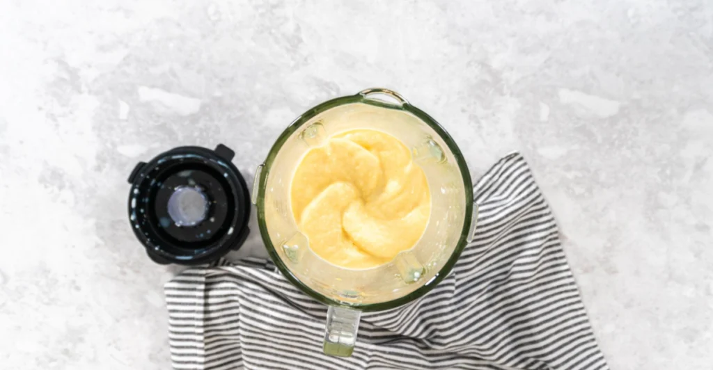 Vista de cima de um liquidificador mostrando a massa lisa e homogênea do queijo vegano de castanha de caju após ser batida.