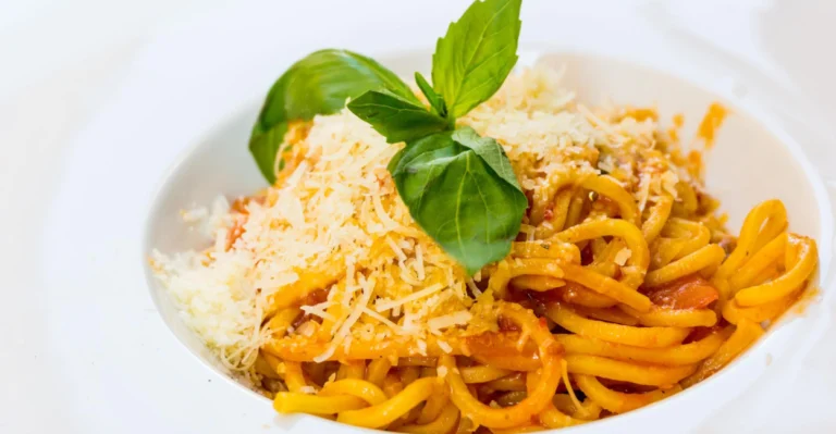 Prato de macarrão com molho de tomate finalizado com queijo parmesão vegano caseiro ralado por cima.