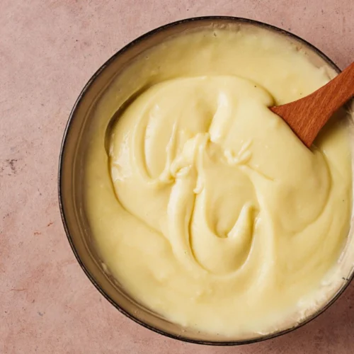 Tigela com queijo vegano de castanha de caju super cremoso e uma espátula de madeira.