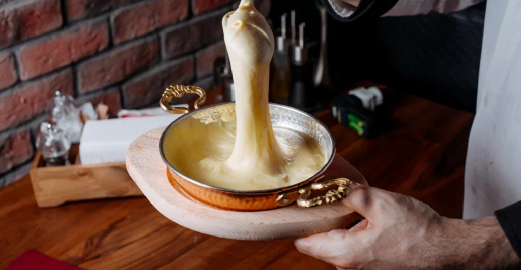 Close-up de um queijo vegano derretido em uma panela, sendo puxado para cima para mostrar sua elasticidade e textura "puxa-puxa