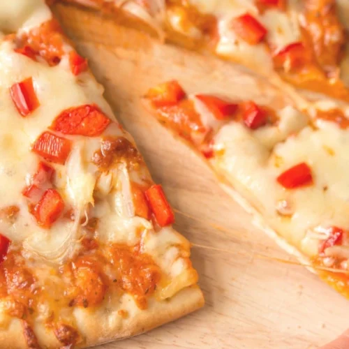 Pizza caseira com mussarela vegana derretida e pimentão vermelho, com uma mão puxando a primeira fatia